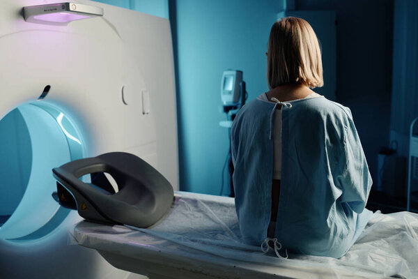 Задний план снимок неузнаваемой женщины в больничном платье, сидящей на современной компьютерной томографии, пространство для копирования