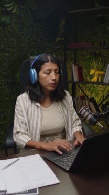 Latin kadın blogcu, kayıt stüdyosunda çalışırken kulaklıkları ayarlarken ve laptop 'da ses podcast' i düzenlerken dikey çekim yapıyor.