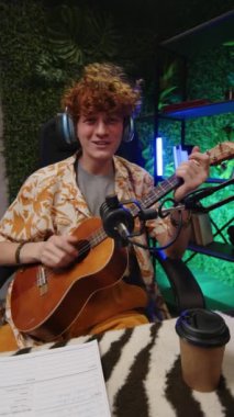 Dikey çekimde, kulaklıklı genç müzisyen kameraya bakıyor, gitar çalıyor ve şarkı söylüyor, sonra stüdyoda sosyal medya blogu için içerik kaydederken arkadaşına beşlik çakıyor.