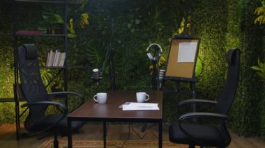 Modern podcast stüdyosunun içinde masada mikrofonlar ve yeşil duvarlar var. Orada kimse yok.