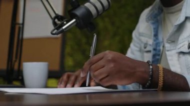 Afrika kökenli Amerikalı podcast sunucusunun yakın görüntüsü elinde kalem tutarken ve mikrofonla konuşurken kayıt stüdyosunda