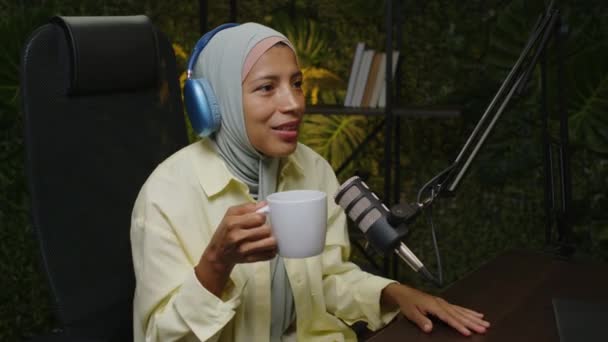 Młoda Blogerka Hidżabie Słuchawki Pijące Herbatę Uśmiechające Się Mówiące Mikrofonie — Wideo stockowe
