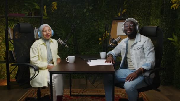 아프리카계 미국인 남성과 히잡에서 마이크와 테이블에 미소와 캐스트 스튜디오에서 카메라에 — 비디오