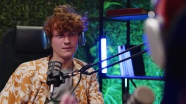 Stüdyoda oturan kıvırcık saçlı, kulaklık takan ve mikrofonla konuşan Z blogcusunun omuzlarının üstünden.