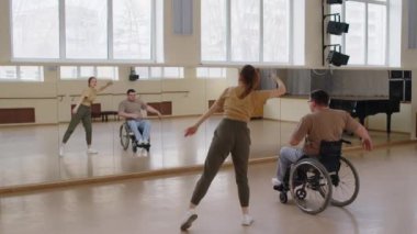 Tekerlekli sandalyedeki genç adam stüdyoda ayna önünde kadın öğretmenle çağdaş dans filmleri yapıyor.