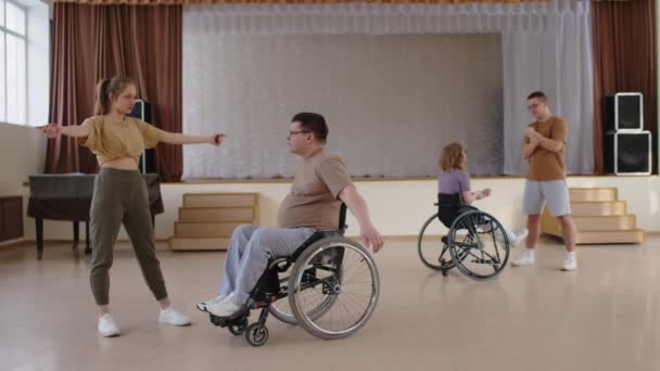 リサイタルホールでリハーサルする前に一緒にウォームアップエクササイズを行う車椅子の若い女性ダンス教師と男性 — ストック動画