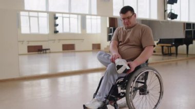 Tekerlekli sandalyedeki genç adam dans dersinden önce ayna duvarlı spor ayakkabıları giyiyor.