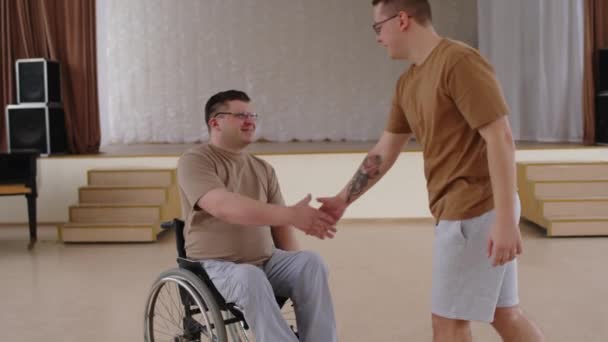 男舞蹈老师与坐在轮椅上的学生握手致意 并在演奏厅与他交谈 — 图库视频影像