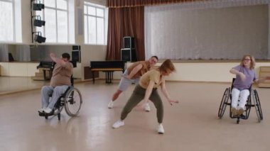 İki profesyonel dansçı ve tekerlekli sandalyedeki kadın ve erkek stüdyoda modern dans gösterisi yapıyorlar.
