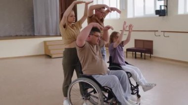 Tekerlekli sandalyedeki genç adam ve kadın stüdyoda dans öğretmenleriyle yeni koreografi öğrenirken çağdaş hareketler yapıyorlar.