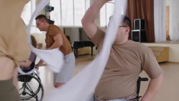 在演播室的舞蹈课上 倾斜拍摄坐在轮椅上的男人和带着白丝带跳舞的女编导的照片 — 图库视频影像