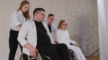 İki tekerlekli sandalye kullanıcısı ve partnerleri konser salonunda sahnede siyah beyaz kıyafetler giyip dans ediyorlar.