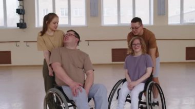 Tekerlekli sandalyede dans stüdyosunda eşleriyle kameraya poz veren neşeli erkek ve kadının grup portresi.