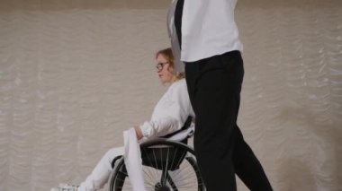 Tekerlekli sandalyedeki kız ve erkek partneri sahnede beyaz kurdeleyle dans ediyor, sonra da gösteriden sonra kameraya poz veriyorlar.