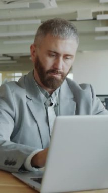 Resmi takım elbiseli bir işadamının ofiste çalışırken bilgisayarda yazarken ve kullanırken dikey görüntüsü.