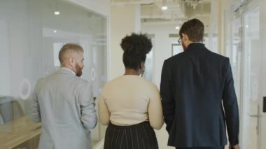 Afrika kökenli Amerikalı bir kadının iki iş ortağıyla modern ofiste koridorda yürümesi ve tartışması.