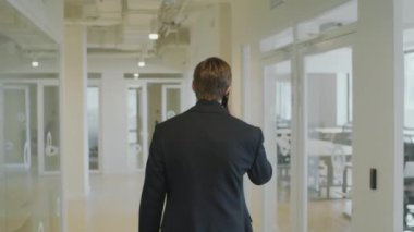 Resmi takım elbiseli bir işadamının ofisteki koridorda yürürken cep telefonuyla konuştuğu arka plan.