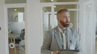 Resmi takım elbiseli bir işadamı, ofisteki koridordan dijital tablet ve oradan geçen iş arkadaşlarını kullanarak geçiyor.