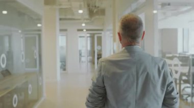 Modern ofis binasında resmi takım elbiseli bir işadamının koridordan geçişi ve iş günlerinde yoldan geçen meslektaşlarını karşılaması.