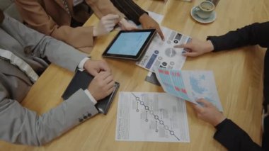 İş ortaklarının dijital tablet ve kağıtlarla ilgili finansal verileri tartışırken ofis ekibinin toplandığı yakın plan çekimleri.