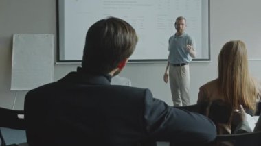 Projeksiyon ekranında duran ve kurumsal seminer sırasında dinleyicilere sunum yapan iş uzmanı