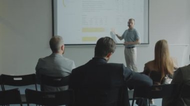 Projeksiyon ekranına mikrofonu olan ve iş konferansı sırasında izleyicilere sunum yapan erkek konuşmacı