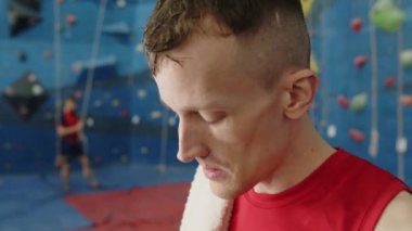 Terli sporcu, spor salonunda antrenman yaptıktan sonra havluyla yüzünü siliyor ve şişeden su içiyor.