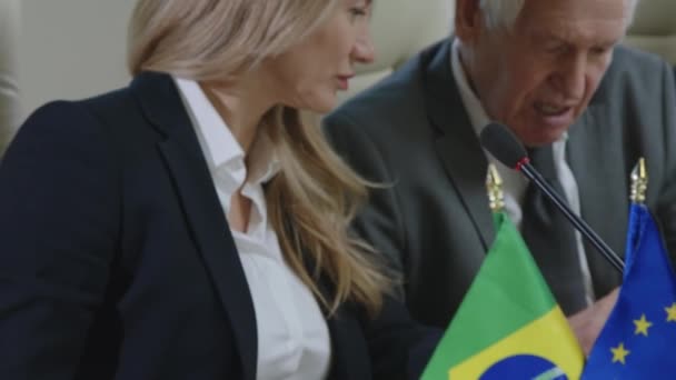 在与欧盟和巴西国旗一起坐在谈判桌前与资深同事讨论的女政治家的倒立镜头 — 图库视频影像