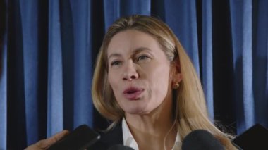 Kadın hükümet yetkilisi basın toplantısı sırasında gazeteciler tarafından tutulan mikrofonlarla gülümsüyor ve konuşuyor