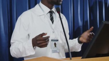 Beyaz önlüklü Afrikalı Amerikalı tıp uzmanının kürsüde kürsüde durup sağlık konferansı sırasında konuşma yapmasını çekin.