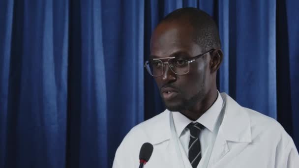 Молодой Афроамериканский Врач Медицинском Халате Стоящий Сцене Выступающий Микрофоне Перед — стоковое видео