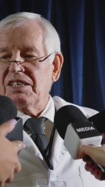 Sağlık sigortası kıdemli uzmanının dikey çekimi etrafında duran ve halka açık etkinlik sırasında mikrofon tutan gazetecilere röportaj vermesi