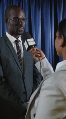 Resmi takım elbiseli Afrikalı Amerikalı politikacının basın konferansında kadın TV muhabirine röportaj yaparken dikey çekimi.