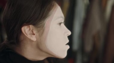 Genç bayan sanatçı, gösteriden önce pandomimci makyajı yaparken yüzüne aşırı beyaz boya sürmek için peçete kullanıyor.