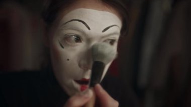 Dişi pandomim sanatçısı sahne performansı için makyajı bitirirken yüzüne beyaz boya sürerek makyaj yapıyor.