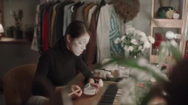 Makyaj yapan genç bir aktris makyaj odasında makyaj masasında otururken fırçayla yüz pudrası uyguluyor ve performansa hazırlanıyor.