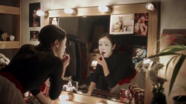Beyaz yüzlü kadın pandomimci, kırmızı ruj sürüyor ve aynaya beyaz bakıyor soyunma odasında tiyatro gösterisi için hazırlanıyor.