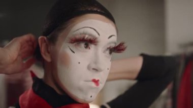 Sahne makyajlı pandomimci kadın. Tiyatroda sahneye çıkmaya hazırlanırken saç filesi takıyor ve takma kirpikleri onarıyor.