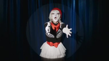 Sahne ışıkları altında poz veren etkileyici kadın pandomimci sahnede doğaçlama yaparken havada öpücükler ve sarılmalar gösteriyor.