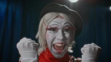 Neşeli kadın pandomimci tiyatro sahnesinde duruyor, kameraya bakıyor, heyecan içinde bağırıyor, dans ediyor ve komedi şovunda başparmağını kaldırıyor.