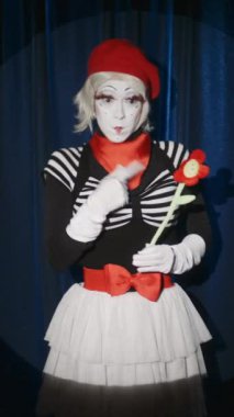 Tiyatroda durup çiçek oyuncağıyla komedi gösterisi yapan komik pandomimci aktrisin dikey çekimi.