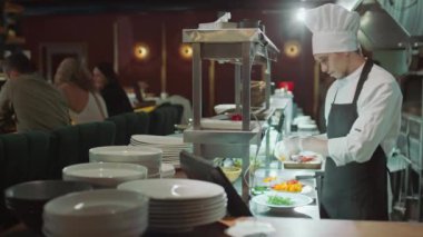 Profesyonel aşçı güzel bir restoranda açık mutfakta yemek pişirirken tabakta salata servis ediyor.