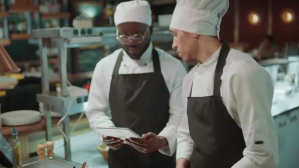 料理長はレストランのキッチンで一緒に作業しながら デジタルタブレットを使用して同僚に仕事を与えます — ストック動画