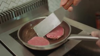 Mutfak spatulasıyla fırında yemek pişirirken tavada biftek çeviren şefin ellerini yakından izle.