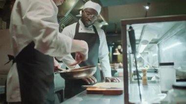 Usta şef, kızarmış et bifteğini cımbızla alıyor ve restoran mutfağında yemek hazırlarken dilimliyor.