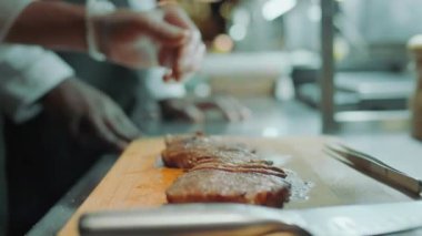 Lokanta mutfağında tabak servis etmeden önce erkek aşçının eldivenli ellerini ahşap tahtaya tuzlu biftek koyarken yakın çekim.