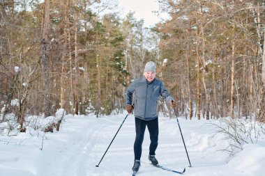 Modern sporcu, yaşlı, beyaz bir adamın kış günü orman yolunda kayak yaparken, kameraya gülümserken, fotokopi çekerken.