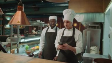 Genç şef cep telefonu kullanıyor, sonra da iş gününün başında restoranda el sıkışarak ve sohbet ederek Afrikalı Amerikalı meslektaşını selamlıyor.