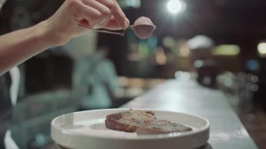 Lokanta mutfağında servis edilen et bifteğine baharat eklerken süzgeç kullanan erkek aşçının yakın plan fotoğrafını çek.