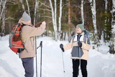 Kafkasyalı turistin elinde akıllı telefon tutarak kış günü karısının Forest Park 'ta fotoğrafını çektiği orta boy bir fotoğraf.